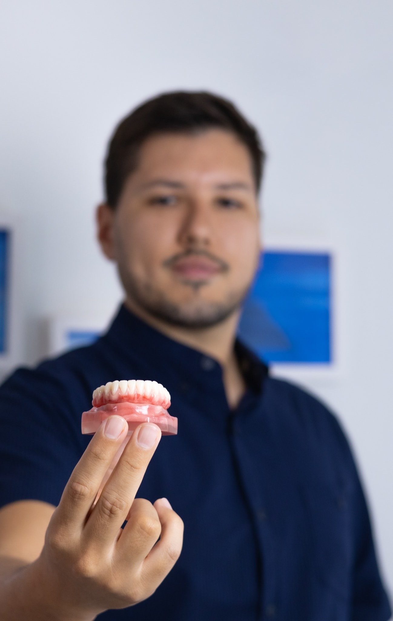 Dr. Murilo Bomfim Alves segurando uma prótese dentária em primeiro plano